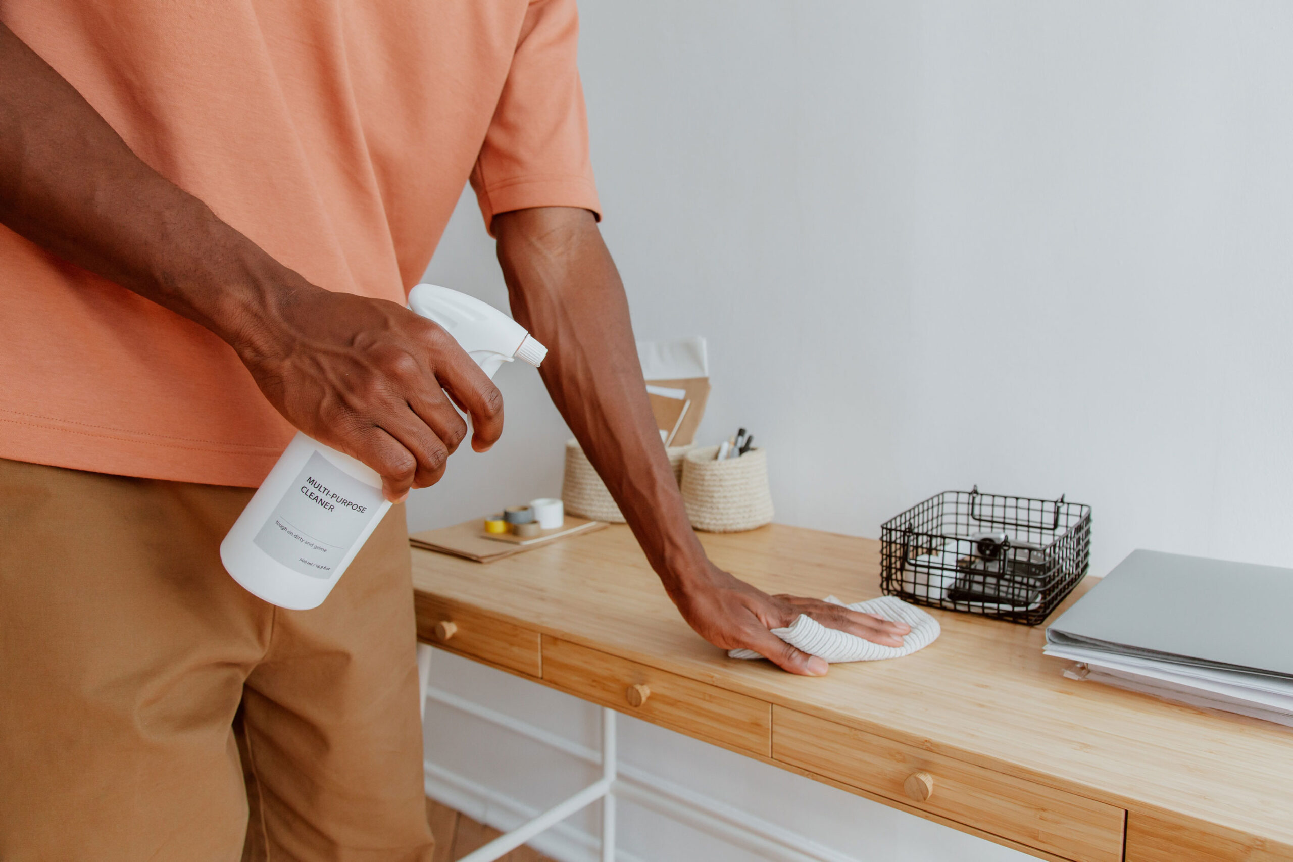 A man using a cloth and spray to clean a side table in a commercial space.